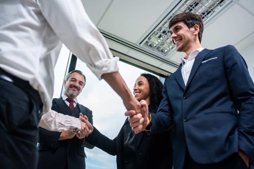 Caucasian businessman making a handshake together while stand in office. Attractive team of employee worker enjoy partnership agreement after negotiations for business deal during working in corporate